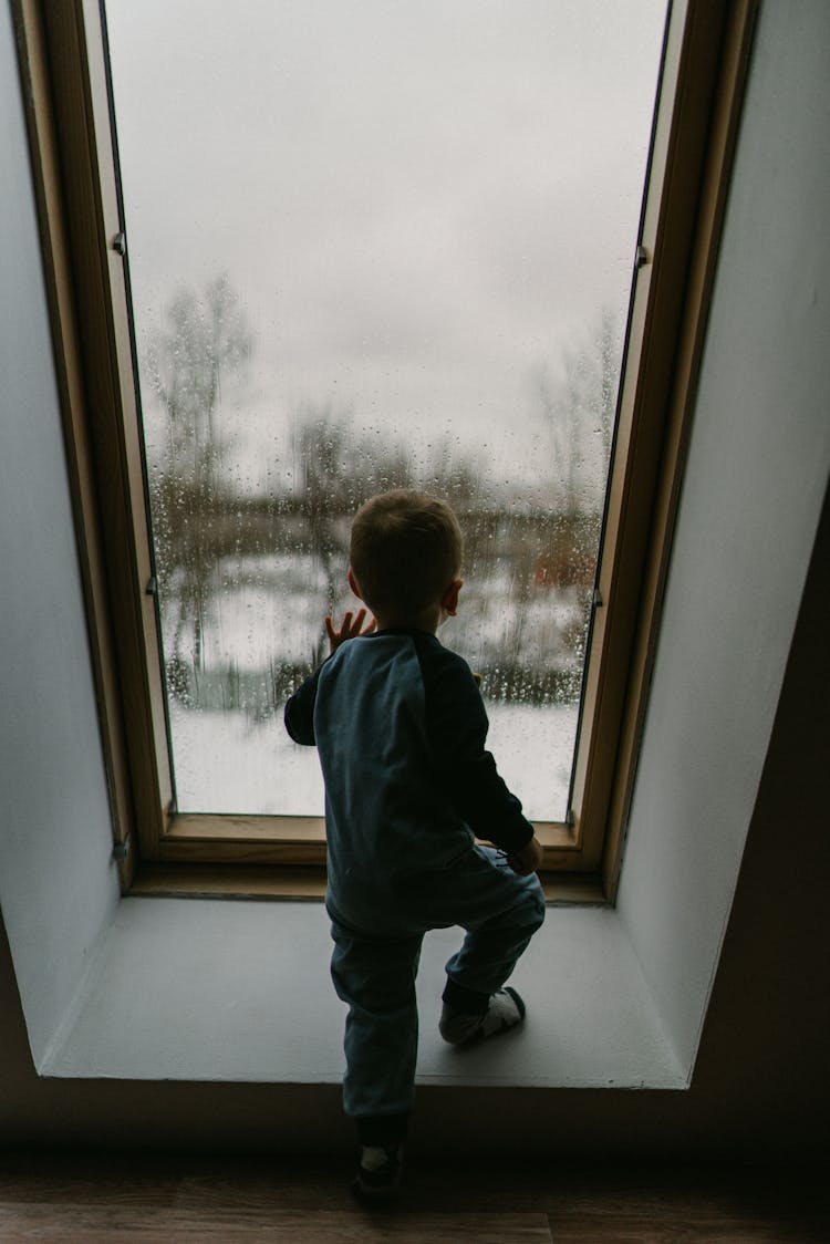 Small Kid Standing Near Window In Winter Day