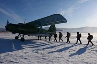 Group of military men in uniform loading into aircraft during test operation in snowy ground of airfield on sunny cold winter day