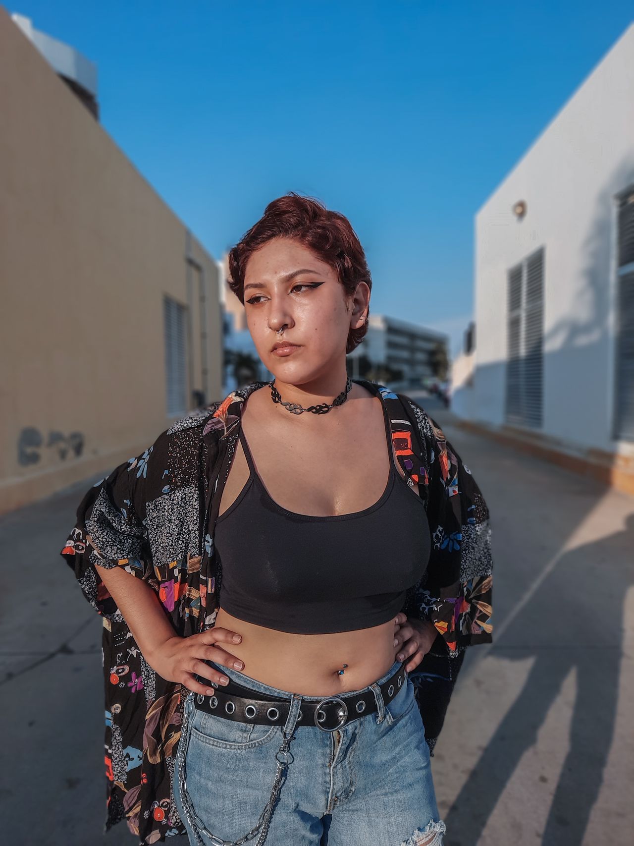 Woman in a black crop top, patterned kimono, and jeans with a grommet belt