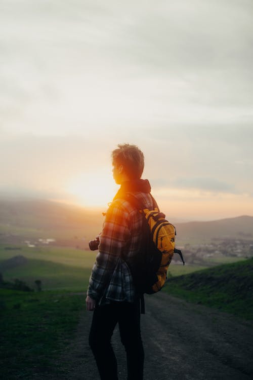 Backpacker contemplating mountains under cloudy sky at sunrise