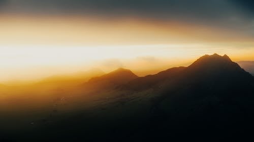 Picturesque view of majestic mount silhouettes under bright cloudy sky illuminated by sunlight in evening