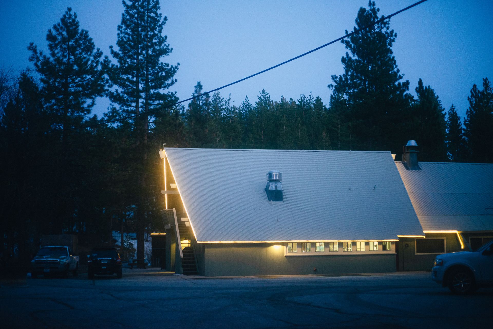 Dwelling building facades with bright lights against overgrown trees under blue sky at dusk in winter town