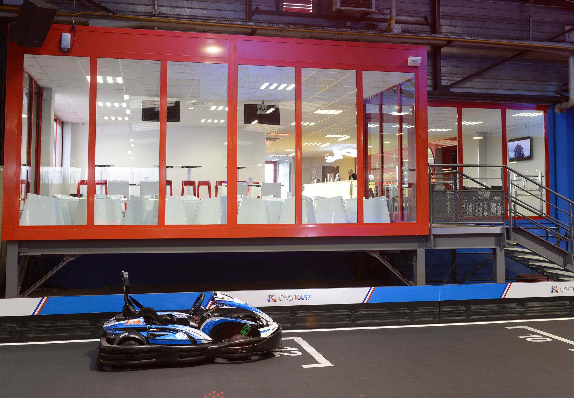 Indoor kart racing track featuring a sleek lounge area with glass windows and modern design.