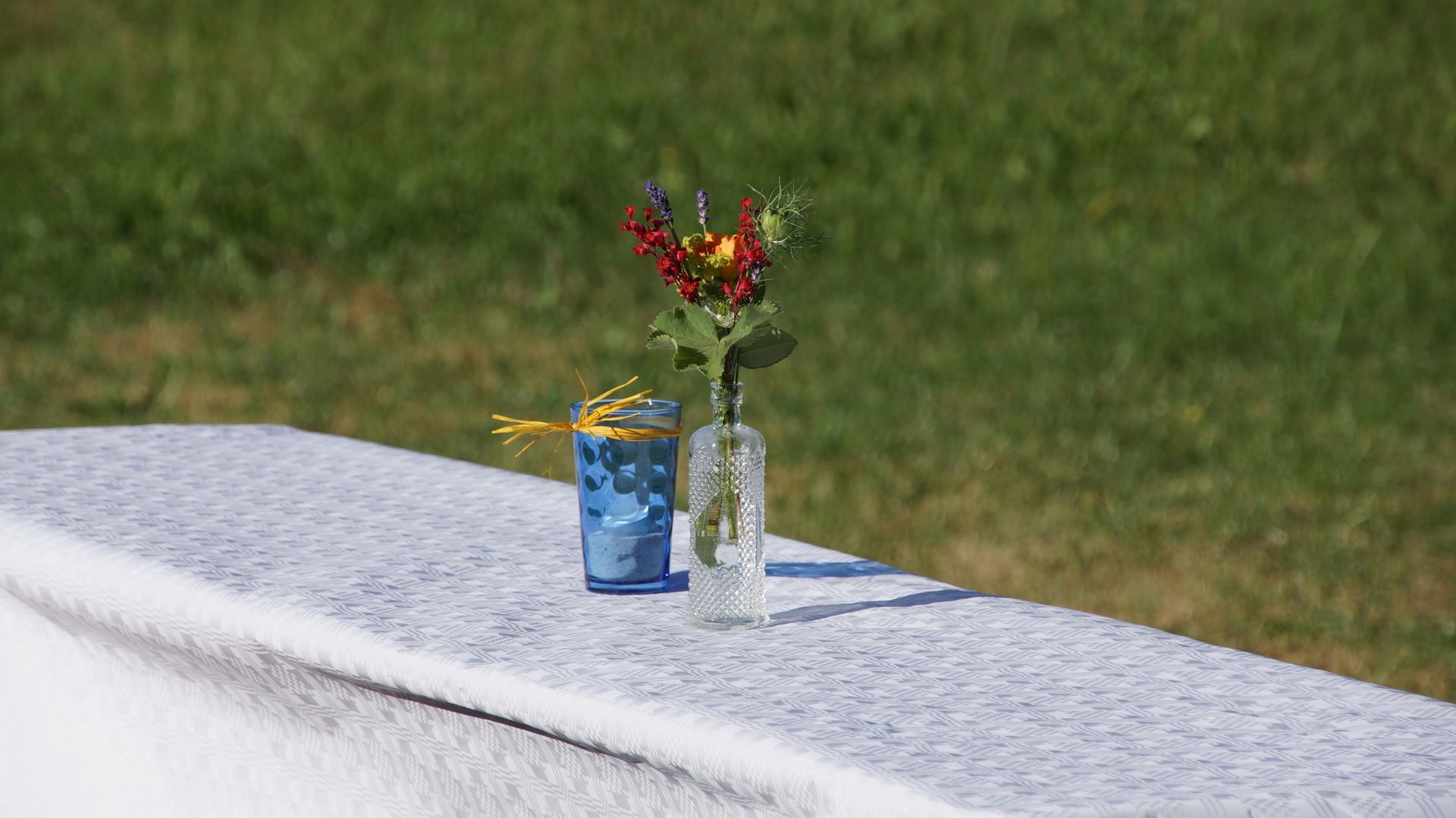 Minimalist outdoor table with a decorative flower vase and glass under sunlight.