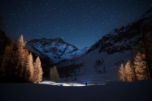 Person Walking on Snow Covered Ground Near Mountain during Night Time