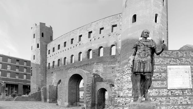 Black and white image of the historic Palatine Gate in Turin, Italy featuring a Roman statue.