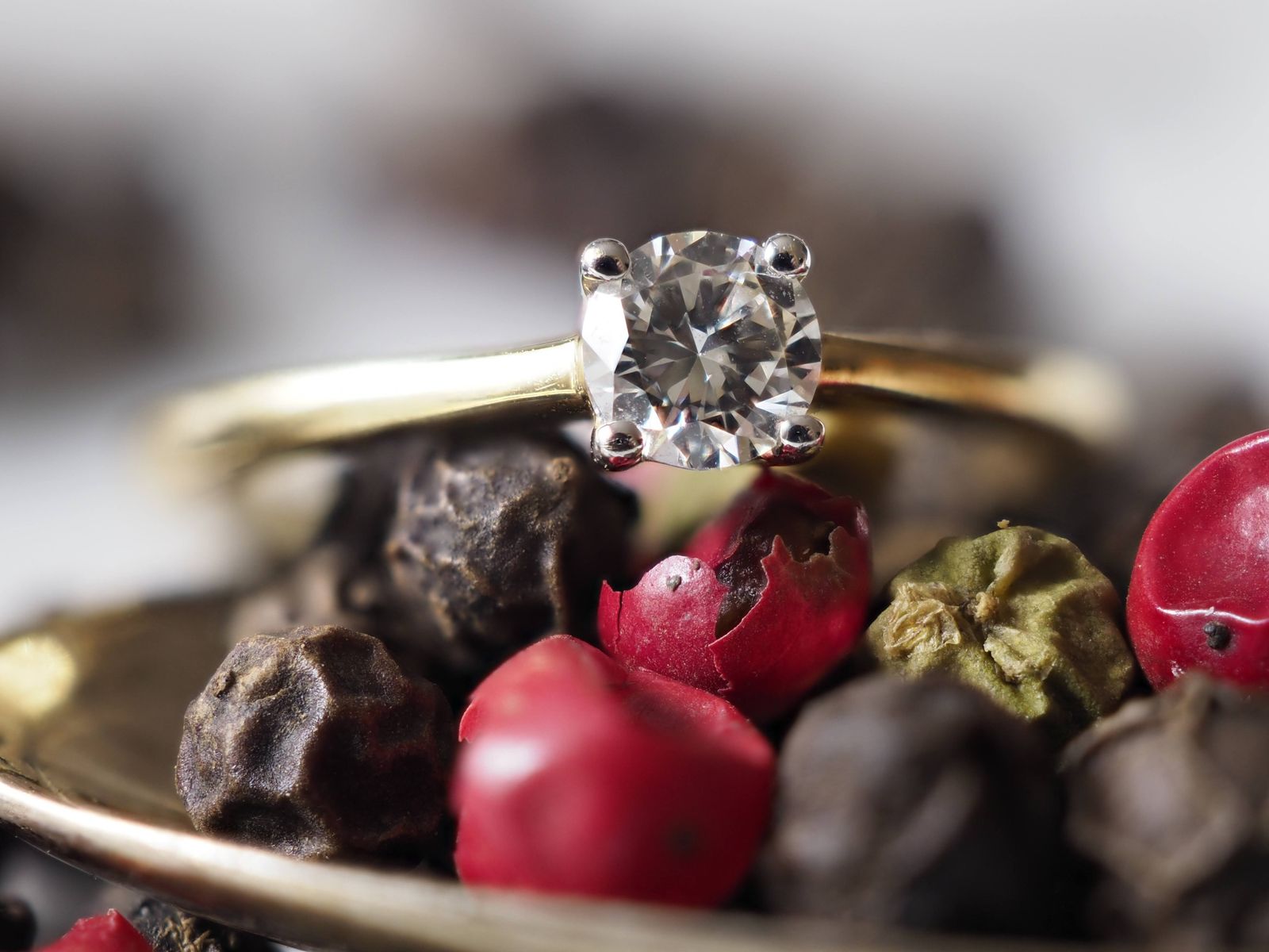 Close-up of a diamond engagement ring placed among colorful peppercorns, creating a luxurious and unique backdrop.