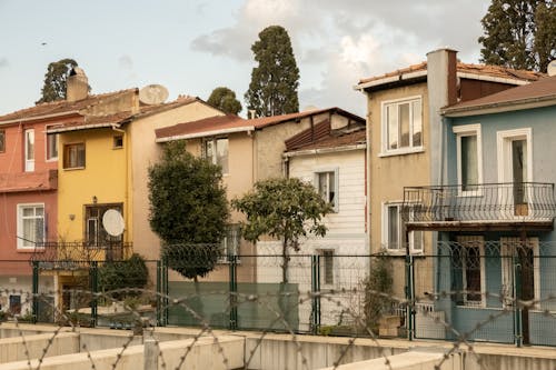 Exterior of residential cottages with small backyards and lush green trees near fence and blue cloudy sky above in port in town