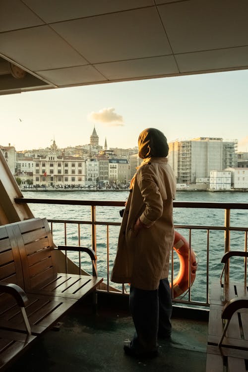 Side view of unrecognizable female traveler in casual clothes standing on deck of cruise boat floating on river and admiring Istanbul at sunset