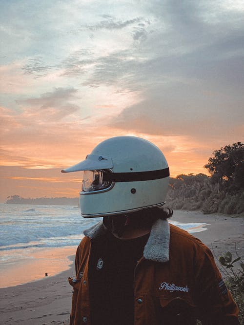 Man Wearing White Motorcycle Helmet on the Beach during Sunset