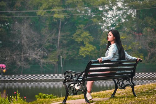 Free A serene moment captured as a young woman sits peacefully on a metal bench by a tranquil lake. Stock Photo