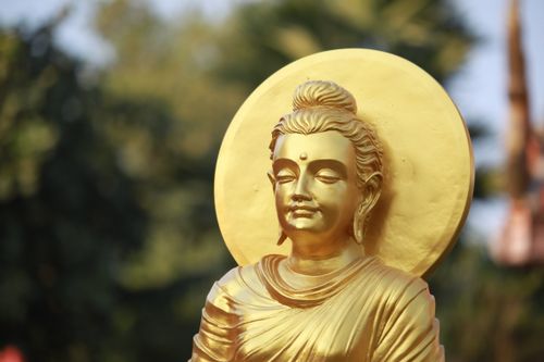 Free Close-up of a golden Buddha statue with a serene expression, sunlit with a blurred background. Stock Photo