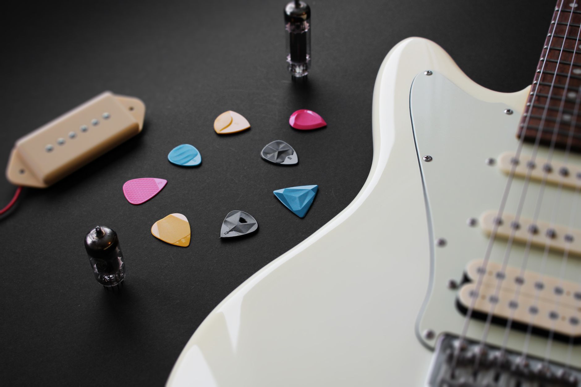 Close-up of an electric guitar with colorful picks and guitar parts on a black surface.