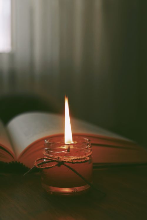 Free Warm candlelight illuminating an open book on a wooden table, evoking a cozy and serene atmosphere. Stock Photo