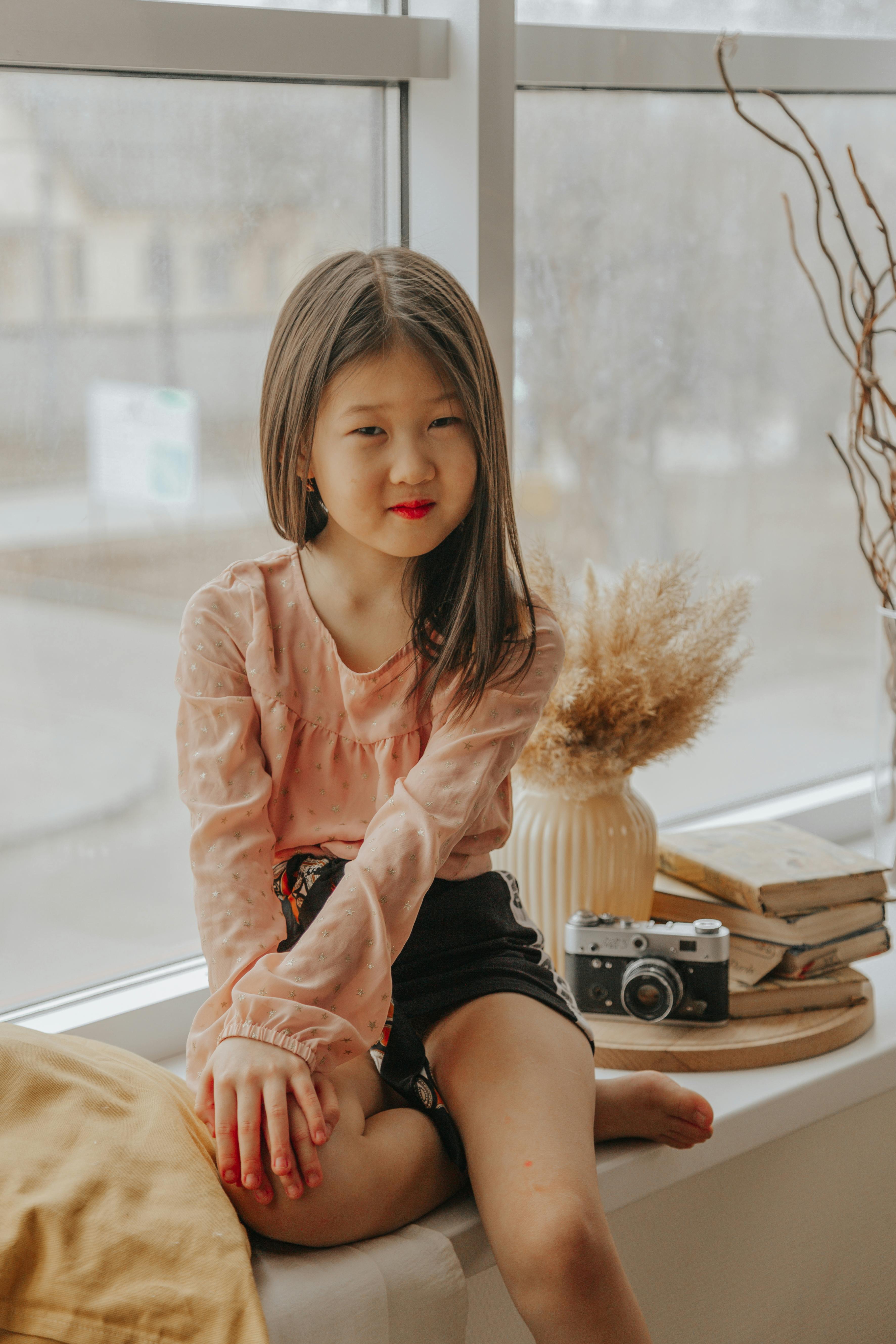 Cute Asian girl sitting on windowsill at home · Free Stock Photo