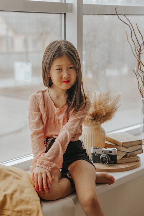 Cute Asian girl sitting on windowsill at home