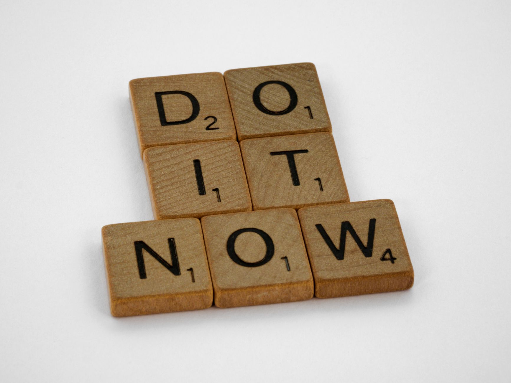 Wooden scrabble tiles forming 'DO IT NOW' on a minimal white backdrop. Inspiring concept.