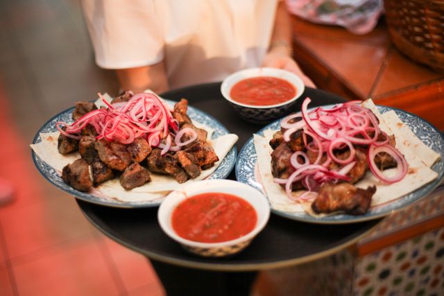 A mouthwatering presentation of grilled meat with onion garnish and sauce bowls.