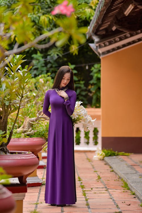 Photo of a Woman in a Purple Dress Posing with Her Hand on Her Chest ...