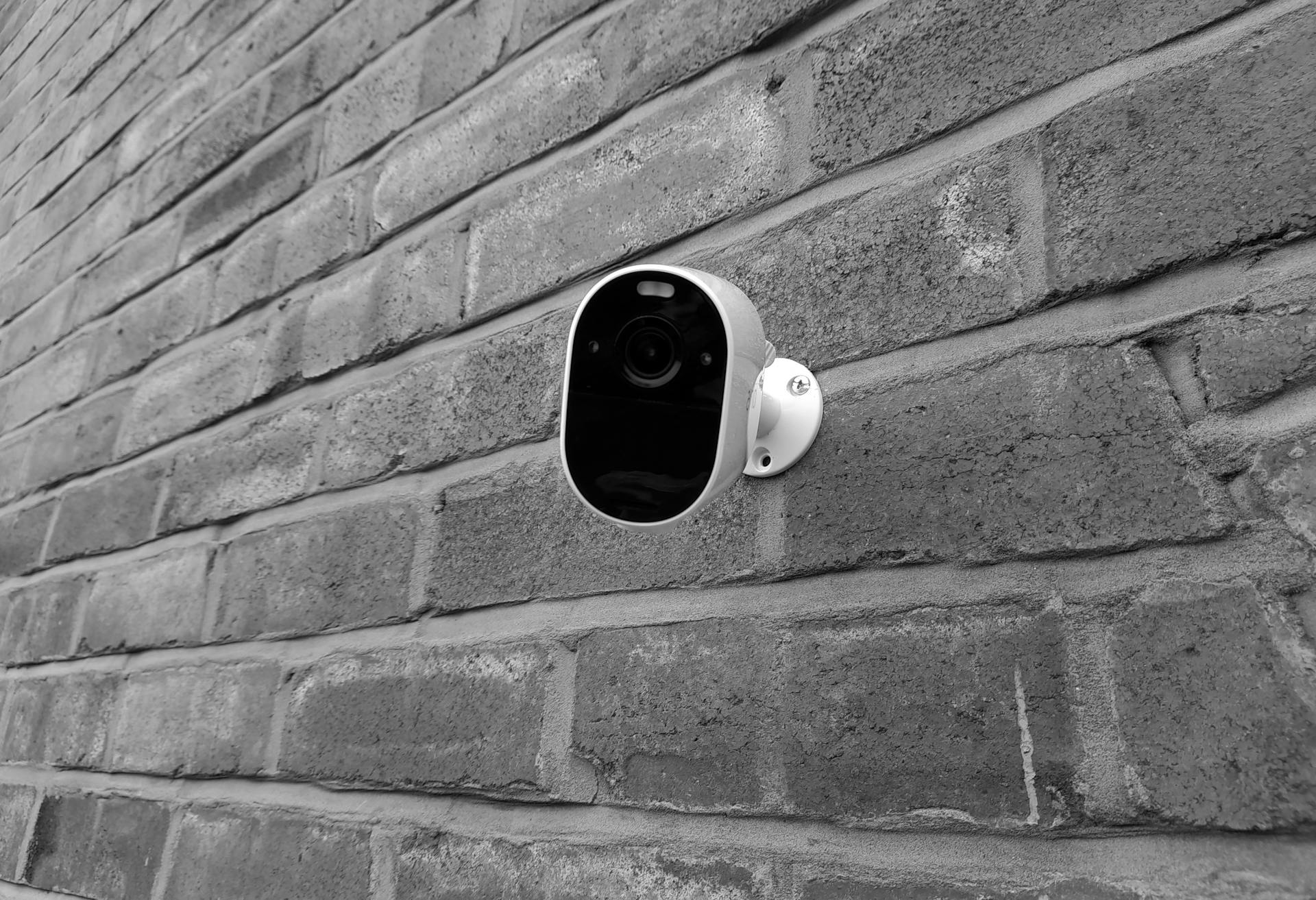 Close-up of a security camera mounted on a brick wall in monochrome.