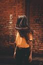 Unrecognizable young female in casual clothes standing on street near brick building while turning head to side on summer day