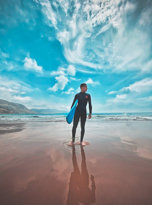 Photo of a Man in a Black Wetsuit Carrying a Blue Surfboard