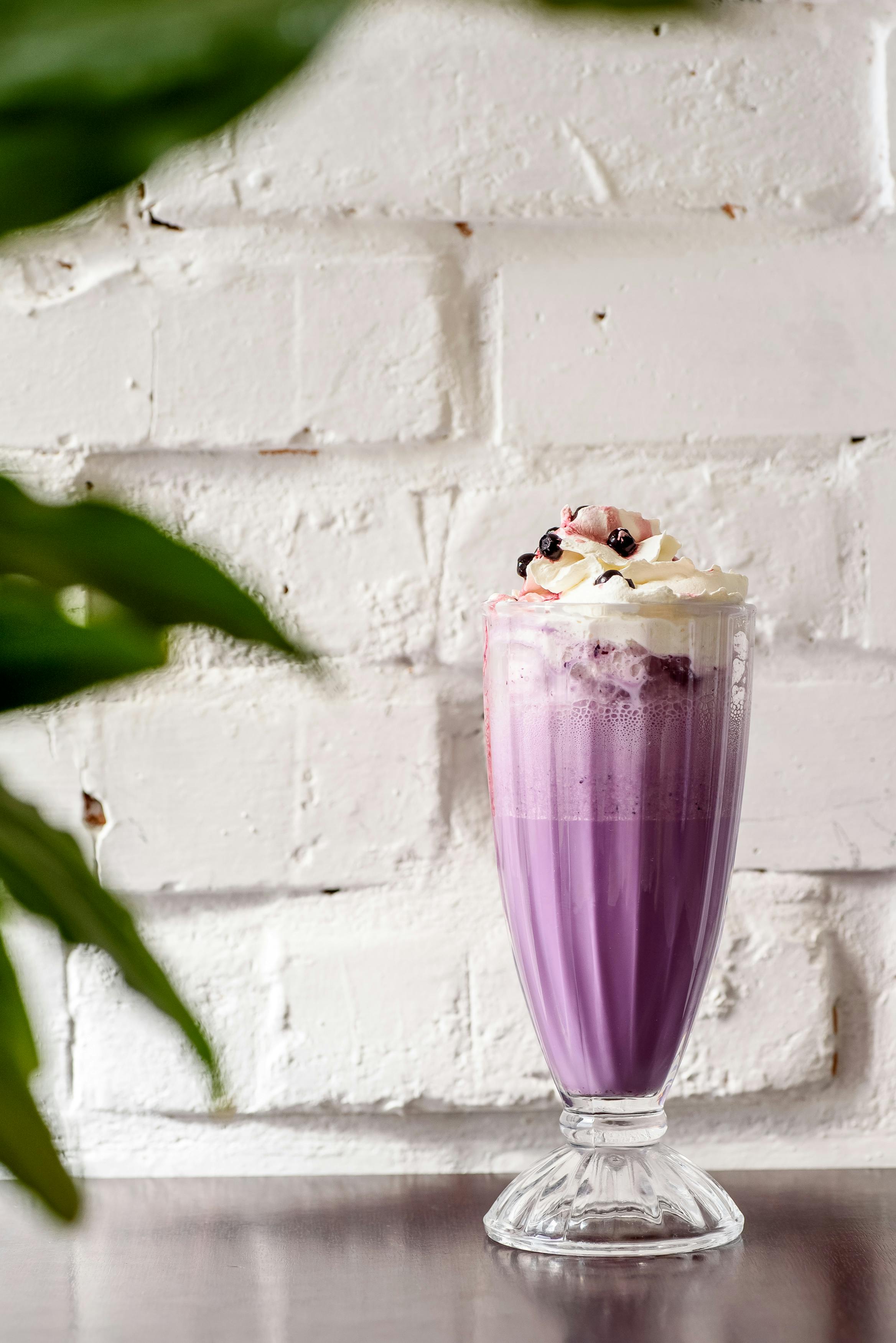 Purple blueberry milkshake with whipped cream against a rustic white brick wall.