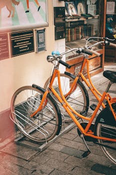 Two vintage orange bicycles are neatly parked on a street in an urban setting, adding a vibrant touch to the scene.