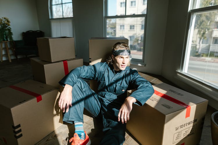 A Man In Blue Jumpsuit Sitting On Brown Boxes