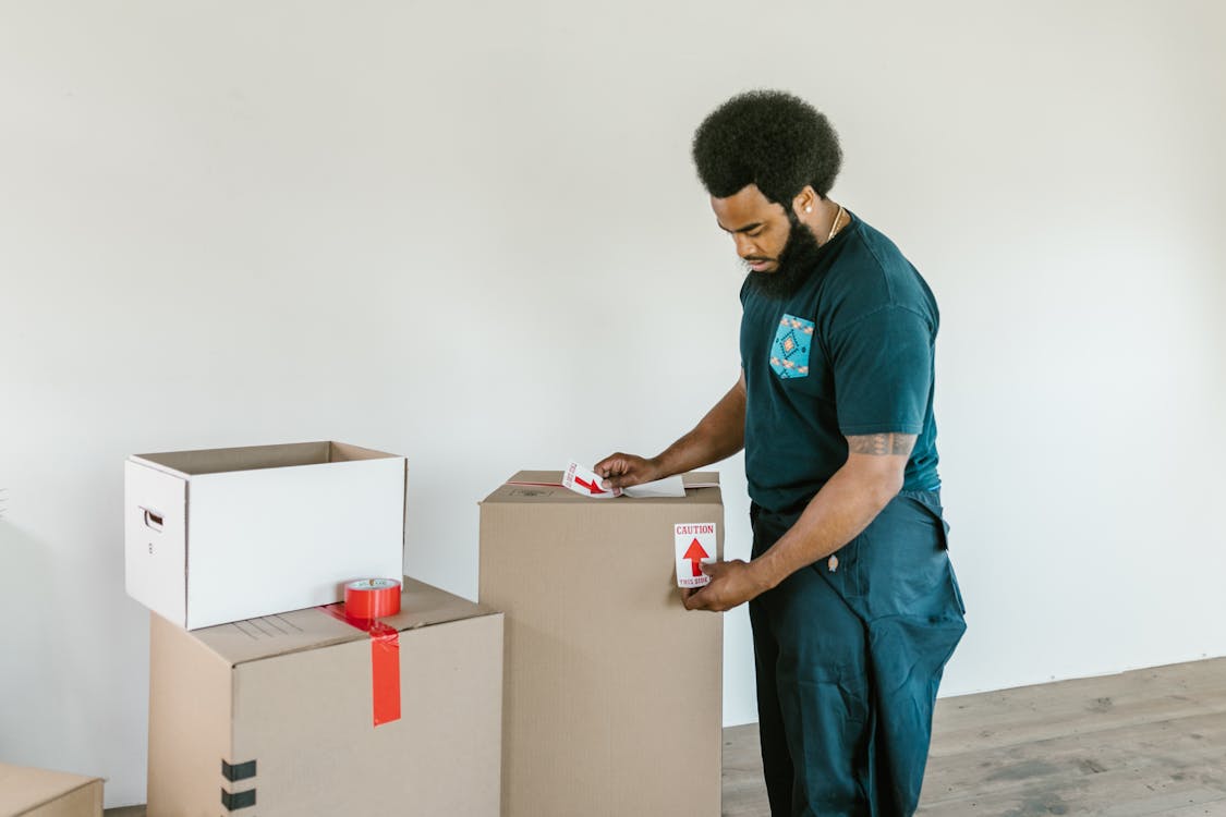 Free Man Putting Caution Stickers on Cardboard Boxes Stock Photo