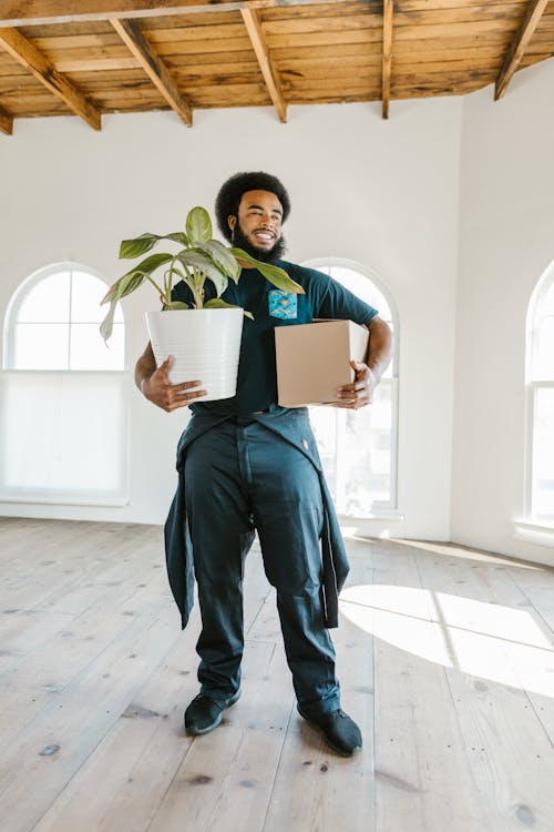 Free A Man Carrying a Potted Plant and a Box while Looking Afar Stock Photo