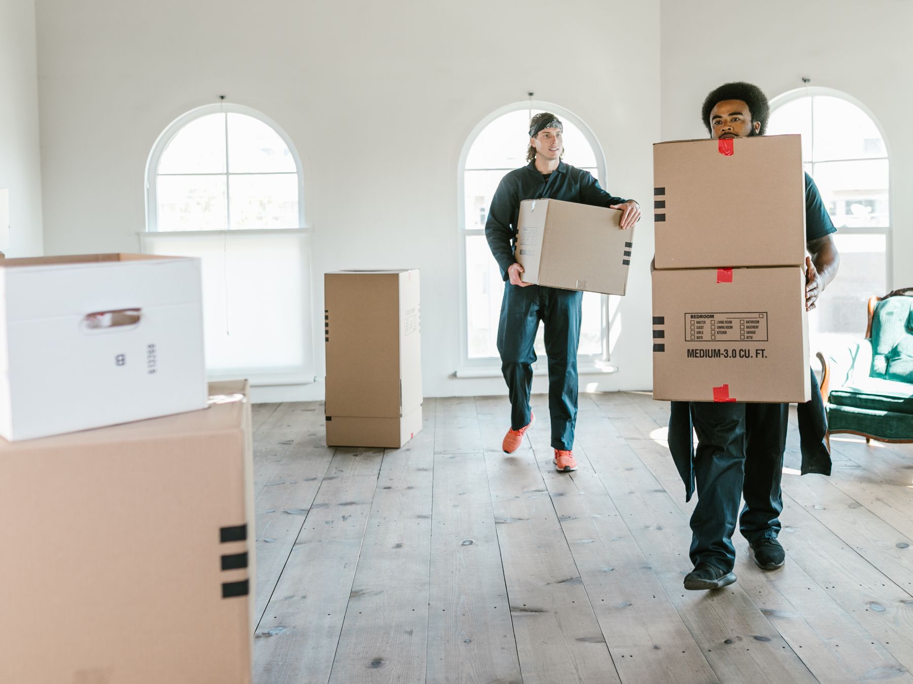 Two friendly movers carrying boxes into a bright, sunlit room
