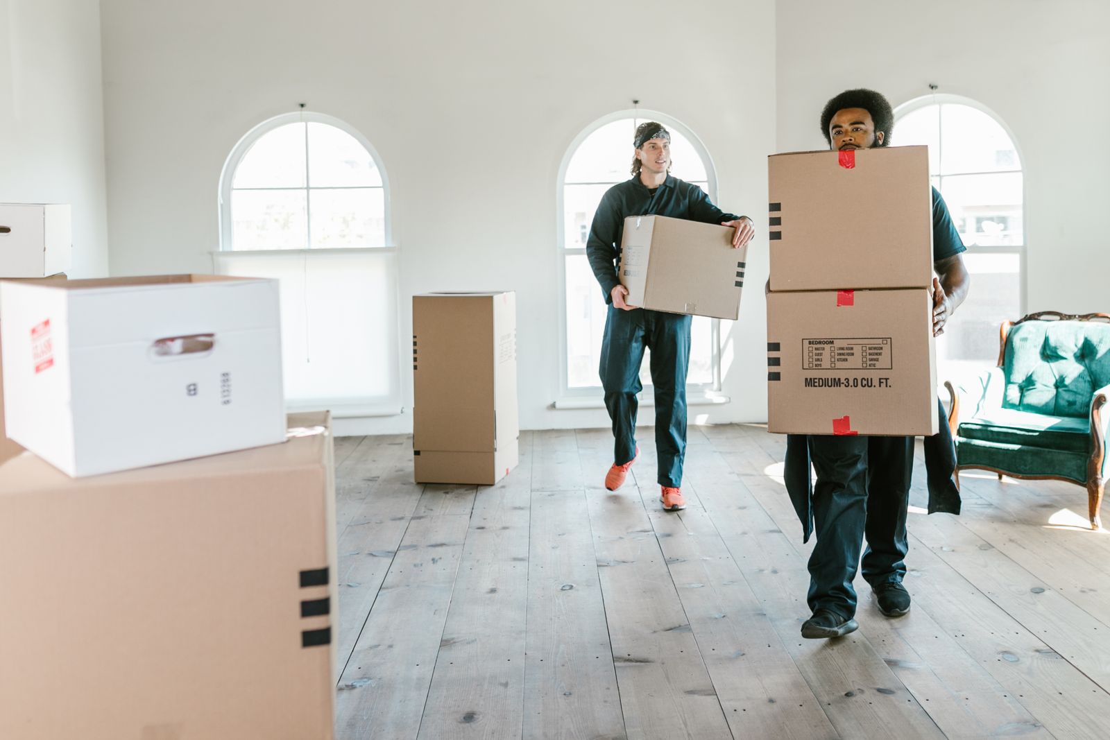 Two movers carrying boxes through a bright room