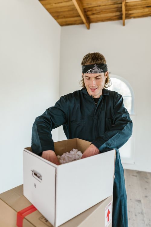 Free Man in jumpsuit packing a cardboard box with foam in a bright room. Stock Photo