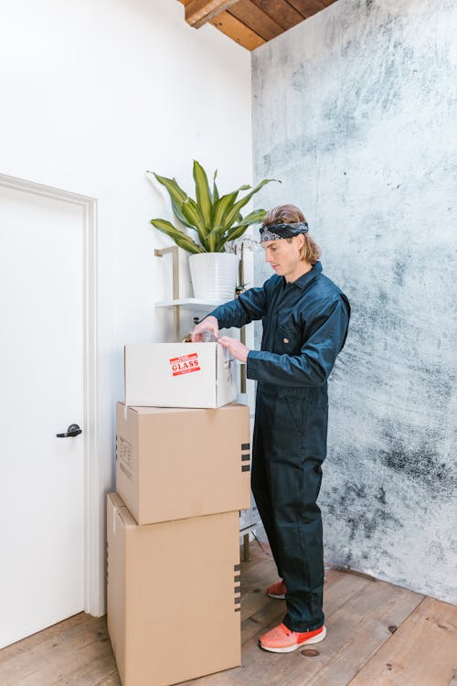Free A Man in Blue Coveralls Near a Stack of Cardboard Boxes Stock Photo