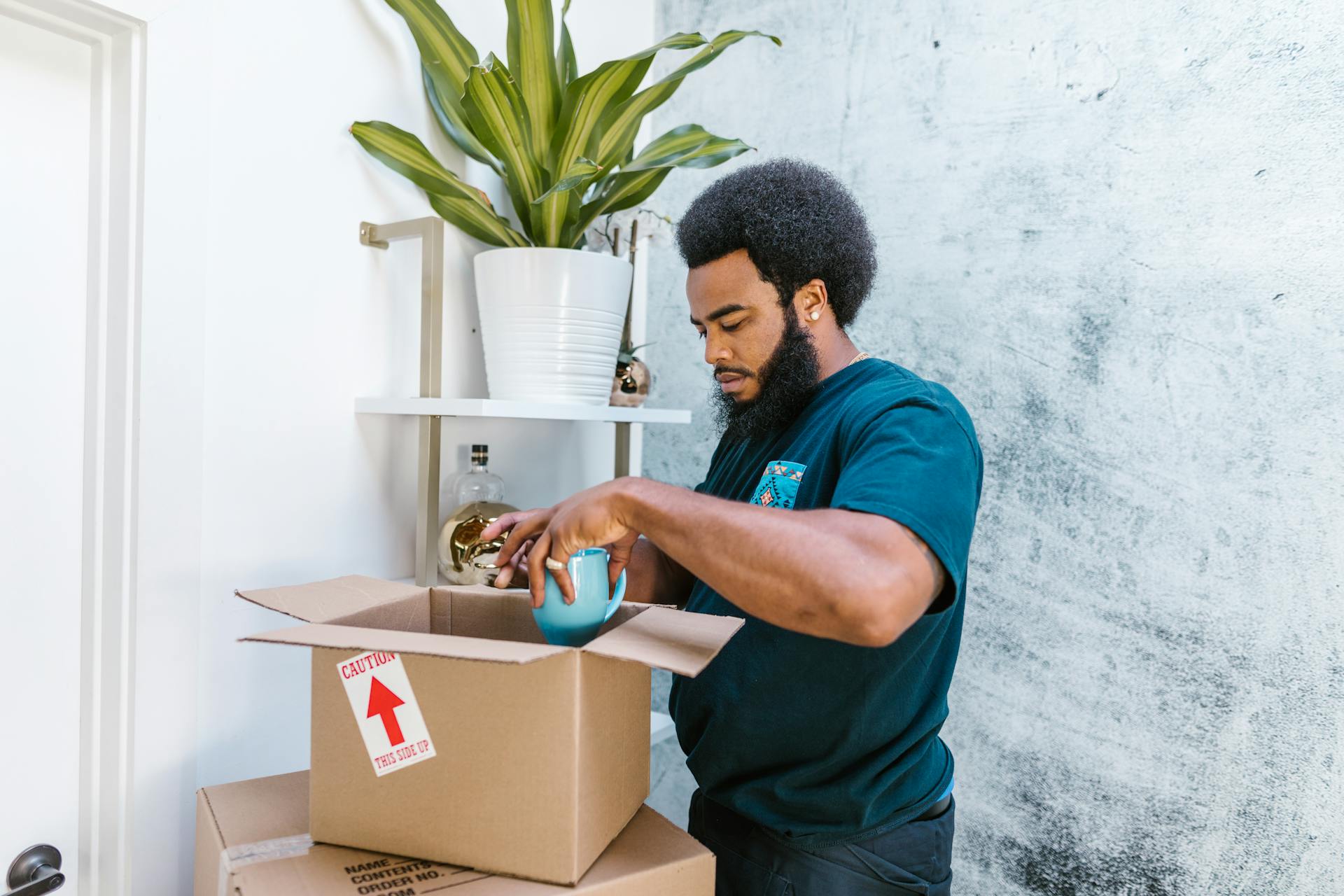 A man packing items into cardboard boxes indoors, preparing for relocation.