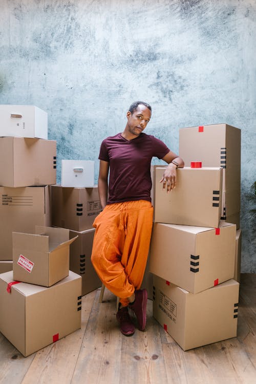 A Man in an Orange Pants Surrounded by Cardboard Boxes