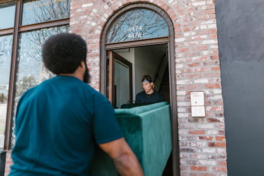 Two men carrying a green sofa into a new home through a brick doorway.