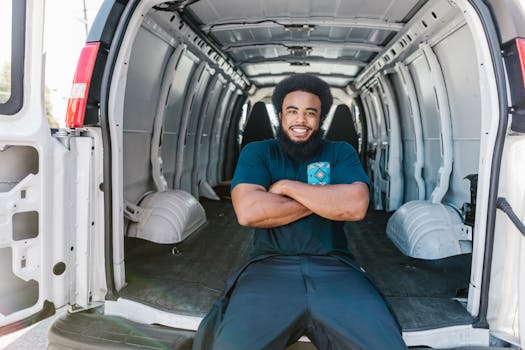 African American man with a beard sitting and smiling inside an empty van, showcasing relaxation and mobility.