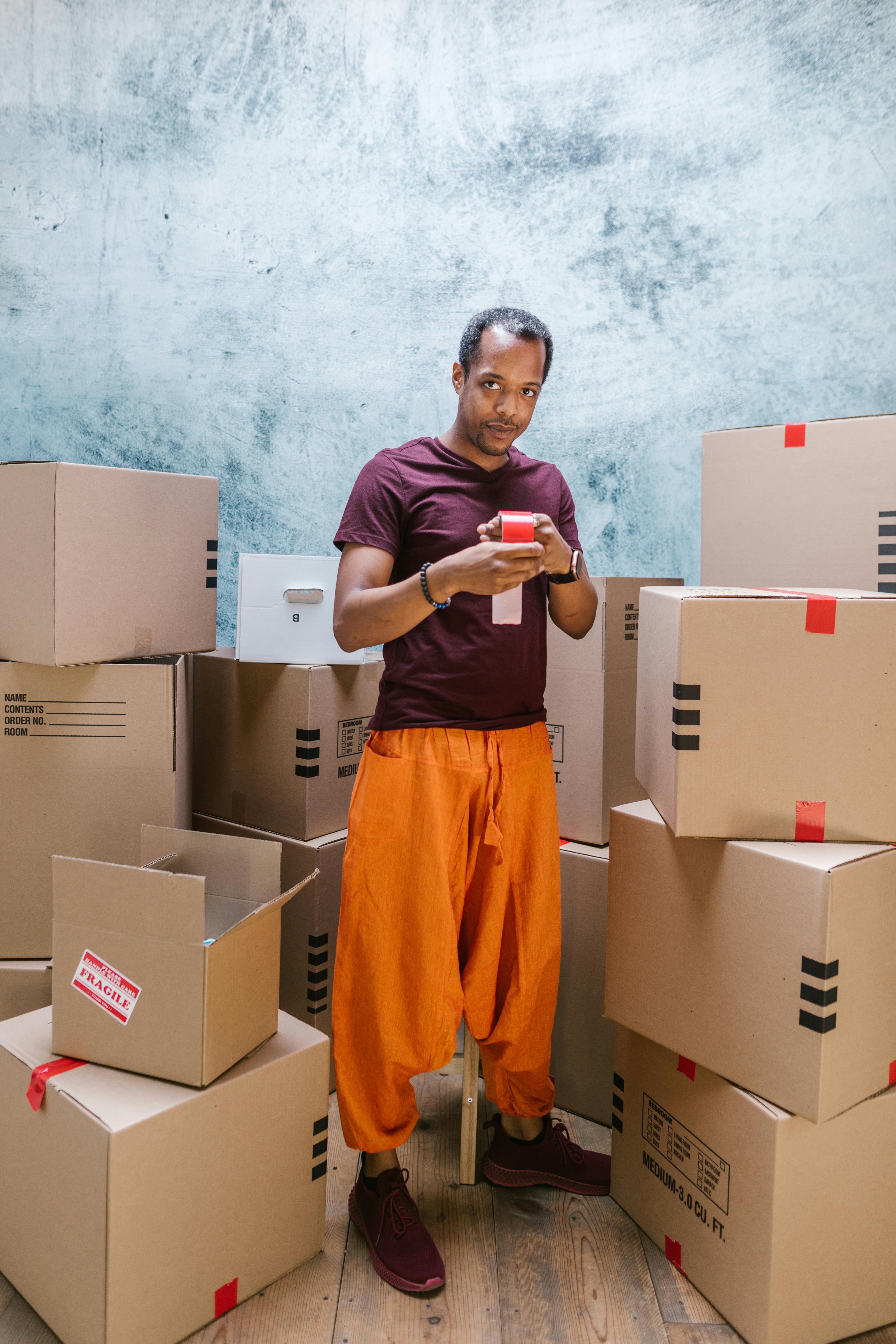 full shot of a man holding atape near cardboard boxes