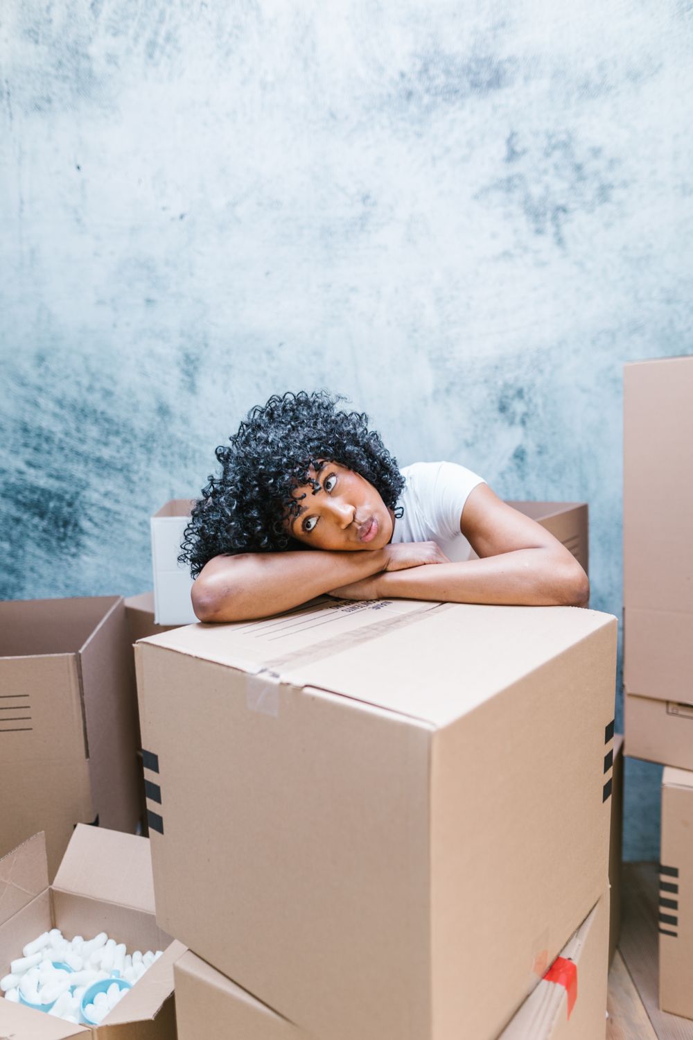 Woman with curly hair resting on cardboard boxes looking contemplative before a move