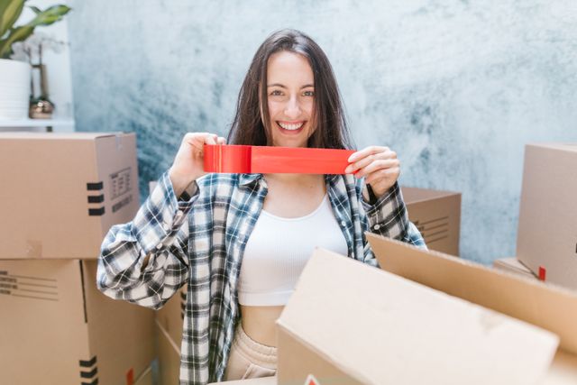 Woman smiling while packing boxes with red tape