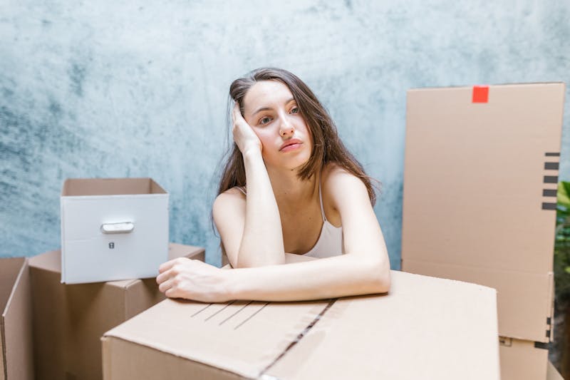 Young woman looking contemplative surrounded by moving boxes indoors.
