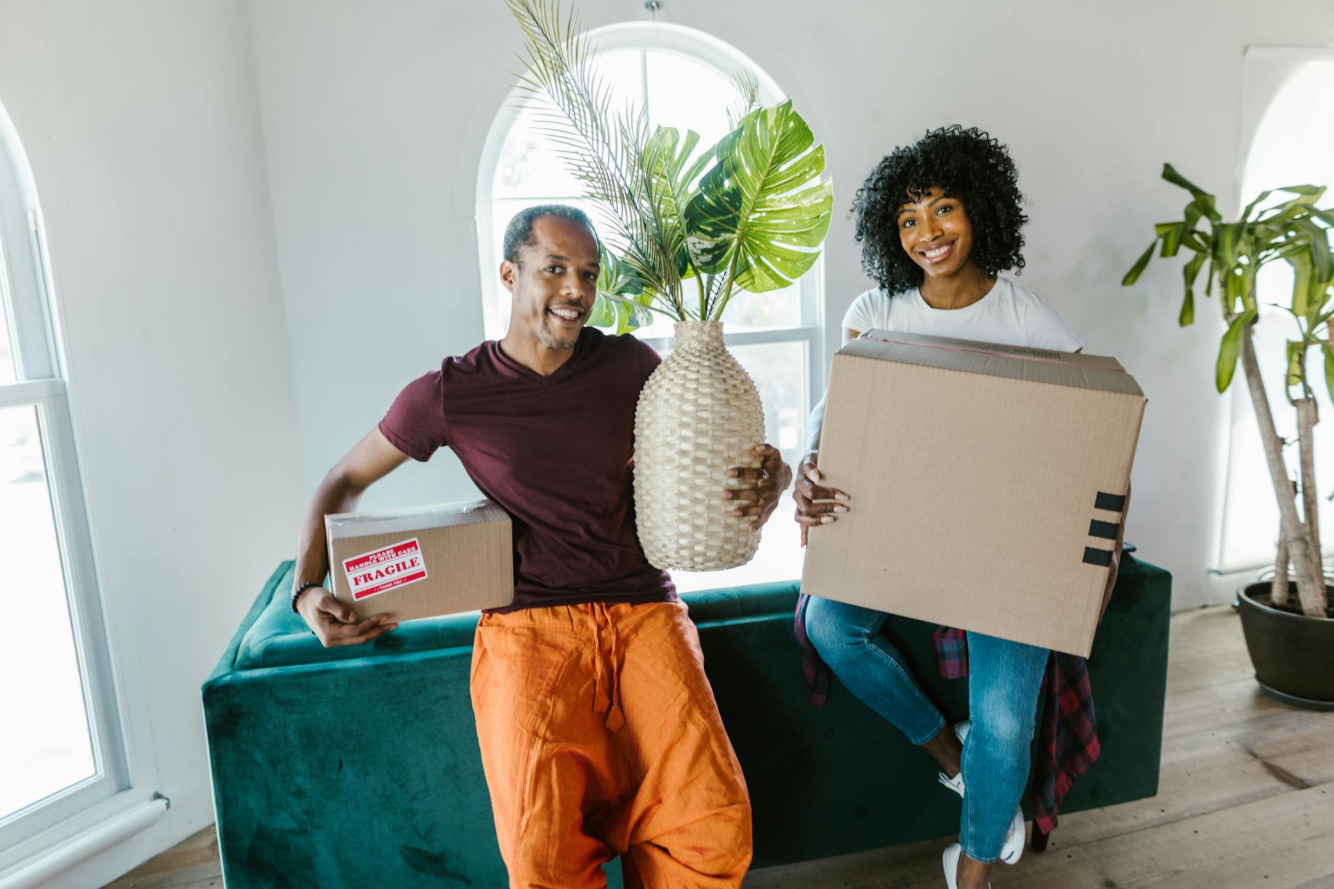 Woman in Purple Long Sleeve Shirt and Orange Pants Holding White Cardboard Box