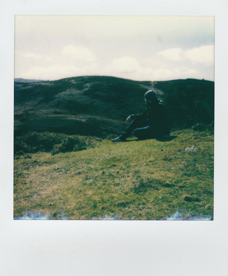 Polaroid Picture Of A Man Sitting On Top Of A Hill 