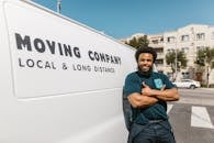 Man in Blue T-shirt and Black Pants Standing Beside White Van