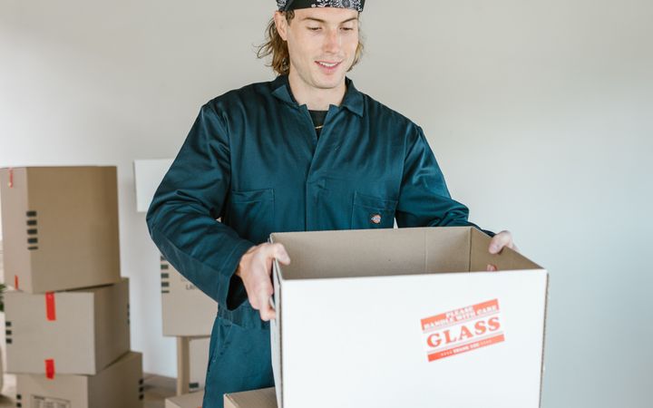 Man in jumpsuit unpacking cardboard boxes in a rustic room during a move.