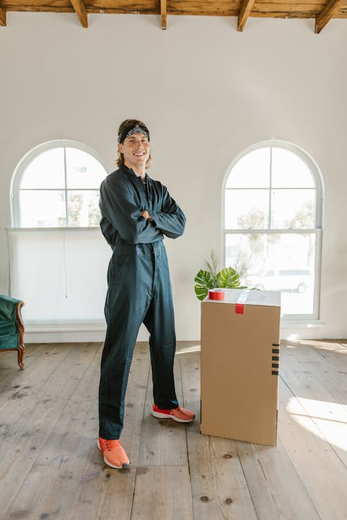 Man With Arms Crossed Standing Beside a Cardboard Box