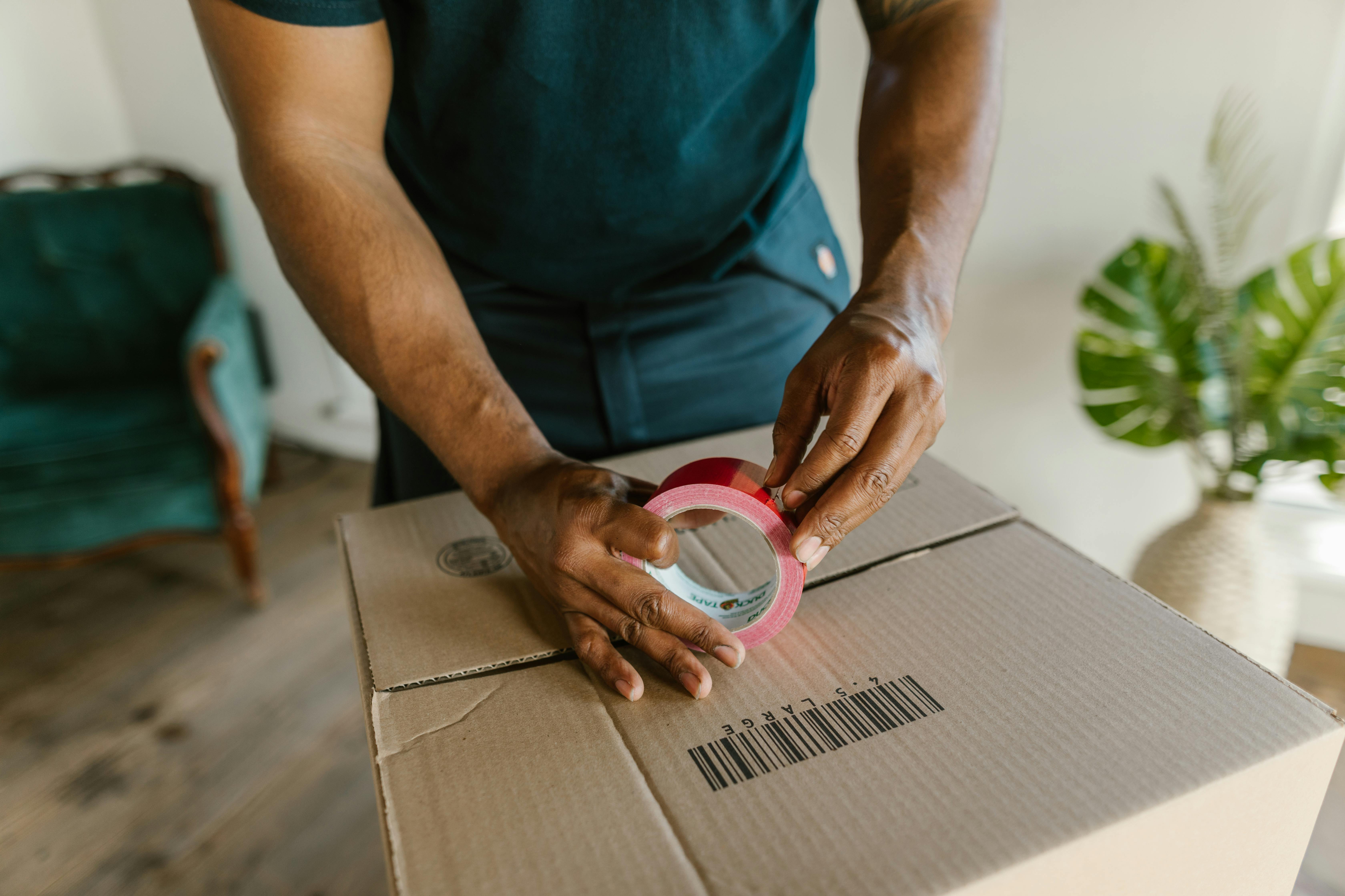 close up shot of a man holding tape on top of a cardboard box