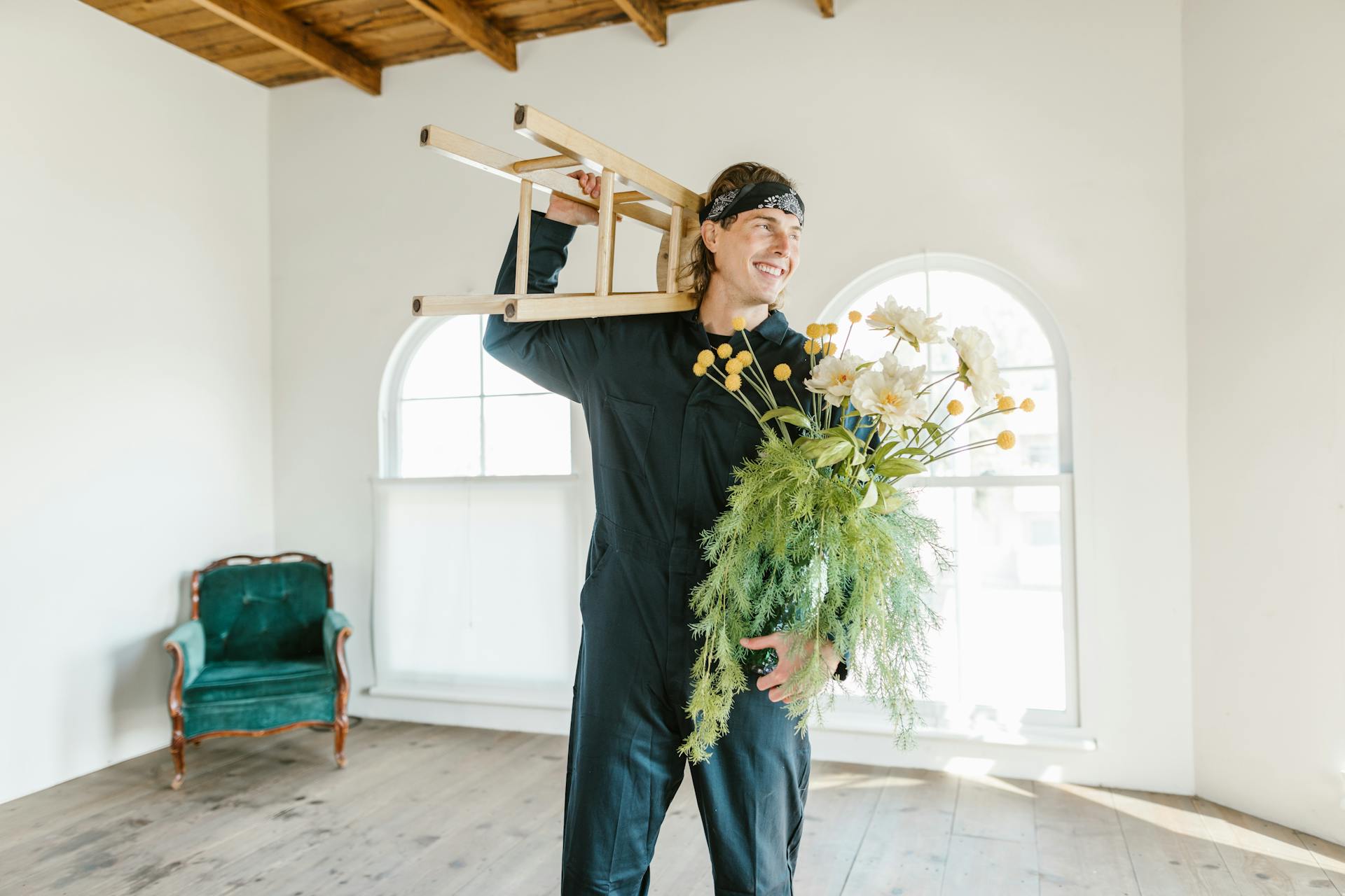Smiling mover in jumpsuit with wooden stool and flower vase indoors